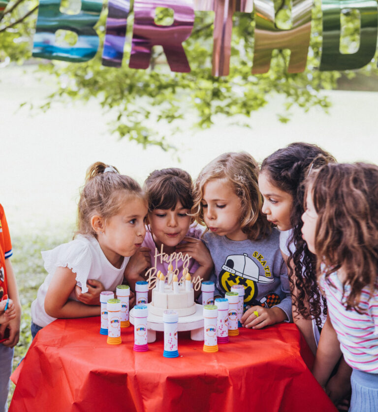 Niños y niñas soplando las velas de una tarta en una de nuestras fiestas infantiles personalizadas, a domicilio.
